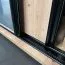 1,1 Meter breiter Schiebetürenschrank Mina in Weiß/Eiche, Metallgriffe in schwarz gehalten, Front aus laminierter Platte, Lamellen in Schwarzer Optik